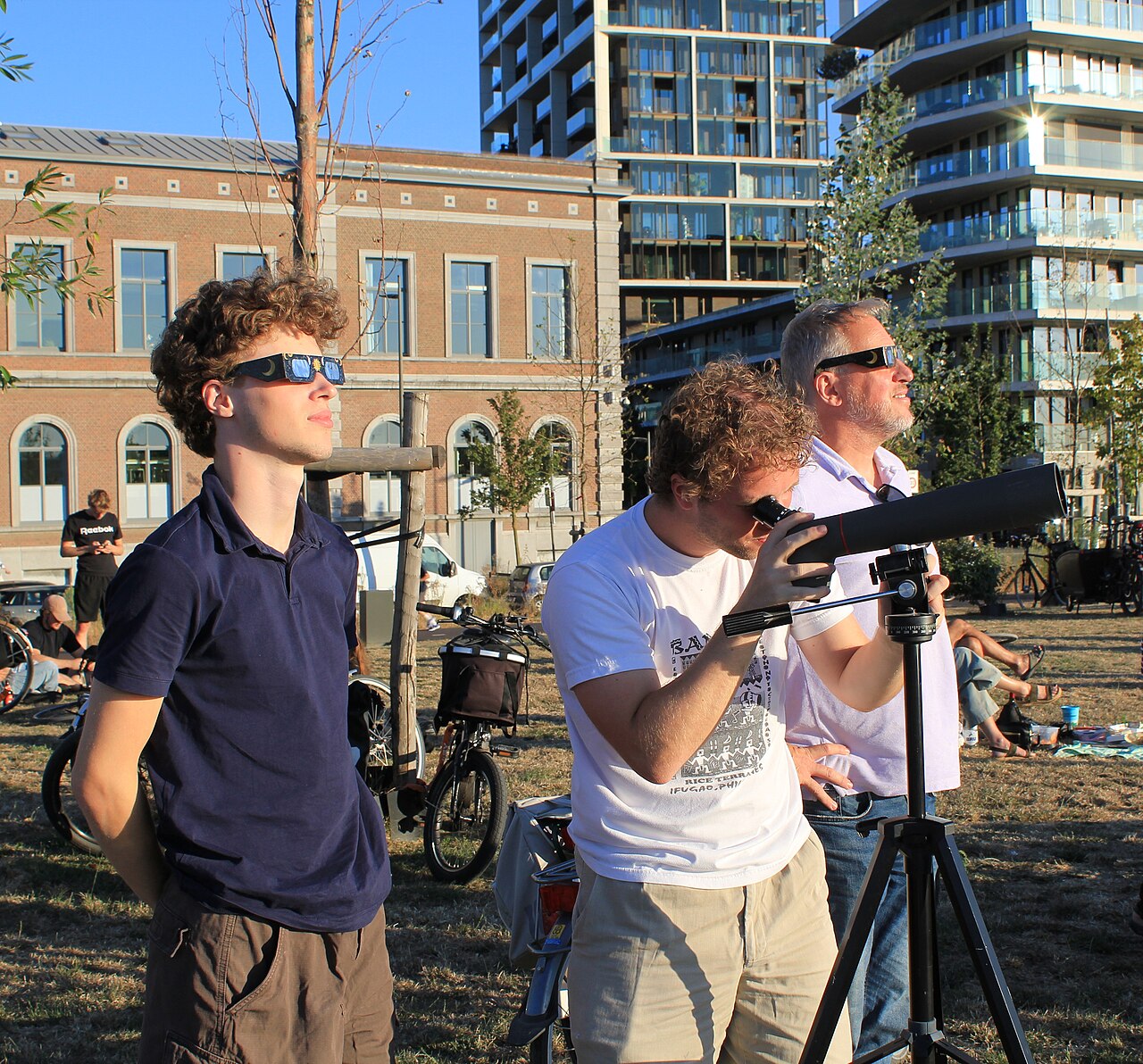 Three people safely watching the solar eclipse with eclipse glasses and a filtered telescope in Antwerp on 12 August 2026